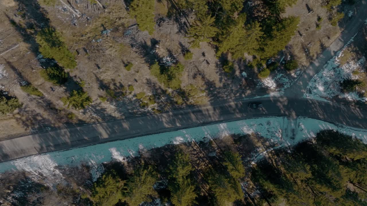 겨울에 지상에 눈이 쌓인 자연이 우거진 소나무 숲을 가로질러 운전하는 모험적인 블랙 suv 자동차를 따라 위에서 아래로 회전하는 공중