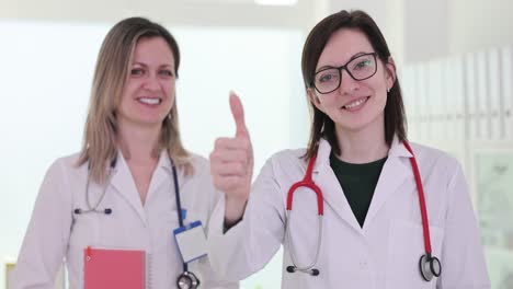 two smiling female doctors in white coats giving a thumbs up