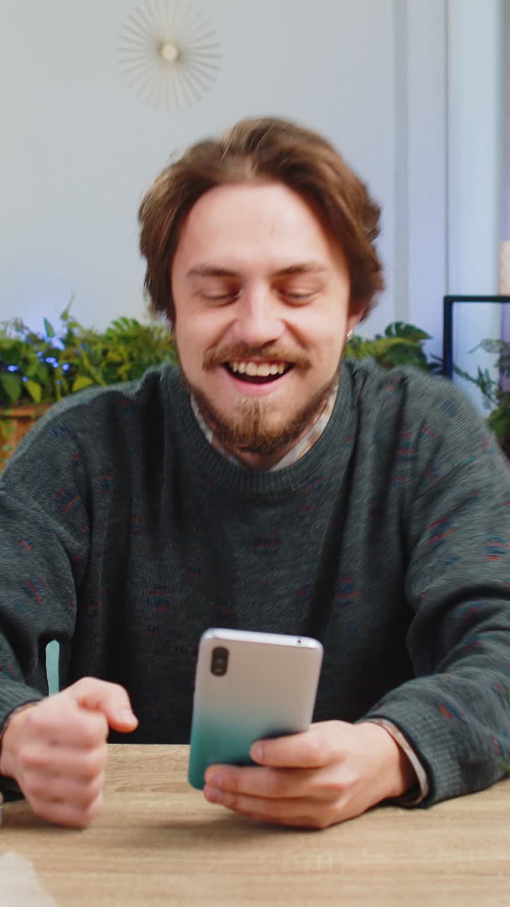 Caucasian man at home table use smartphone celebrating success victory winning play online game