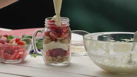 assembling dessert - applying cream from a piping bag to fresh strawberries in a jar