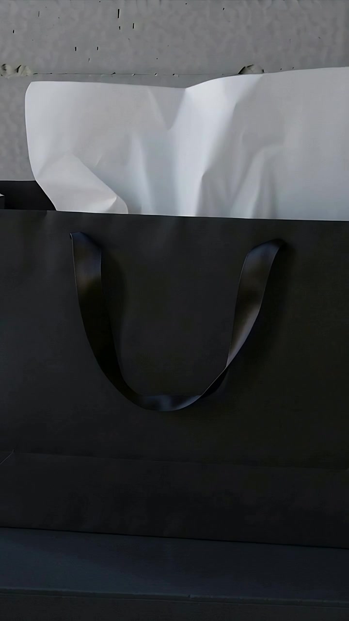 Video verticale: Sacchetto di carta nero su una sporgenza, una brezza leggera solleva la carta velina bianca rivelando i manici in raso