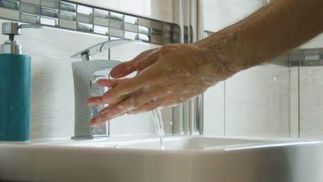 male rinsing soap off of hands and arms close up in a bathroom sink in super slow motion