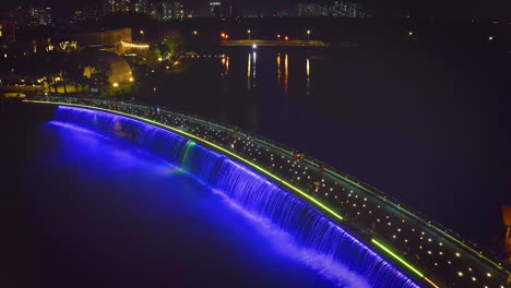 wide aerial crane shot of starlight bridge or anh sao bridge at night, a pedestrian bridge with colored lights and waterfall in district 7 of ho chi minh city or saigon, vietnam