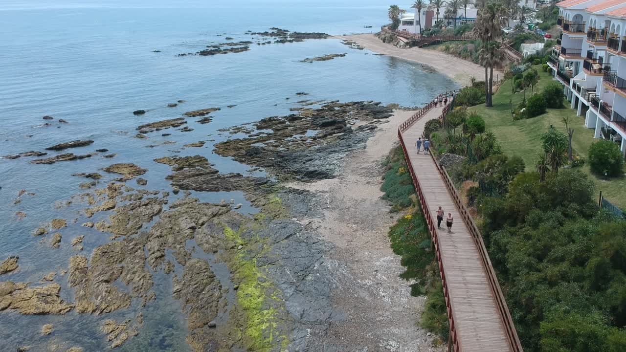 caminos de madera en una playa tranquila con gente paseando por el camino en un pueblo costero en málaga, españa