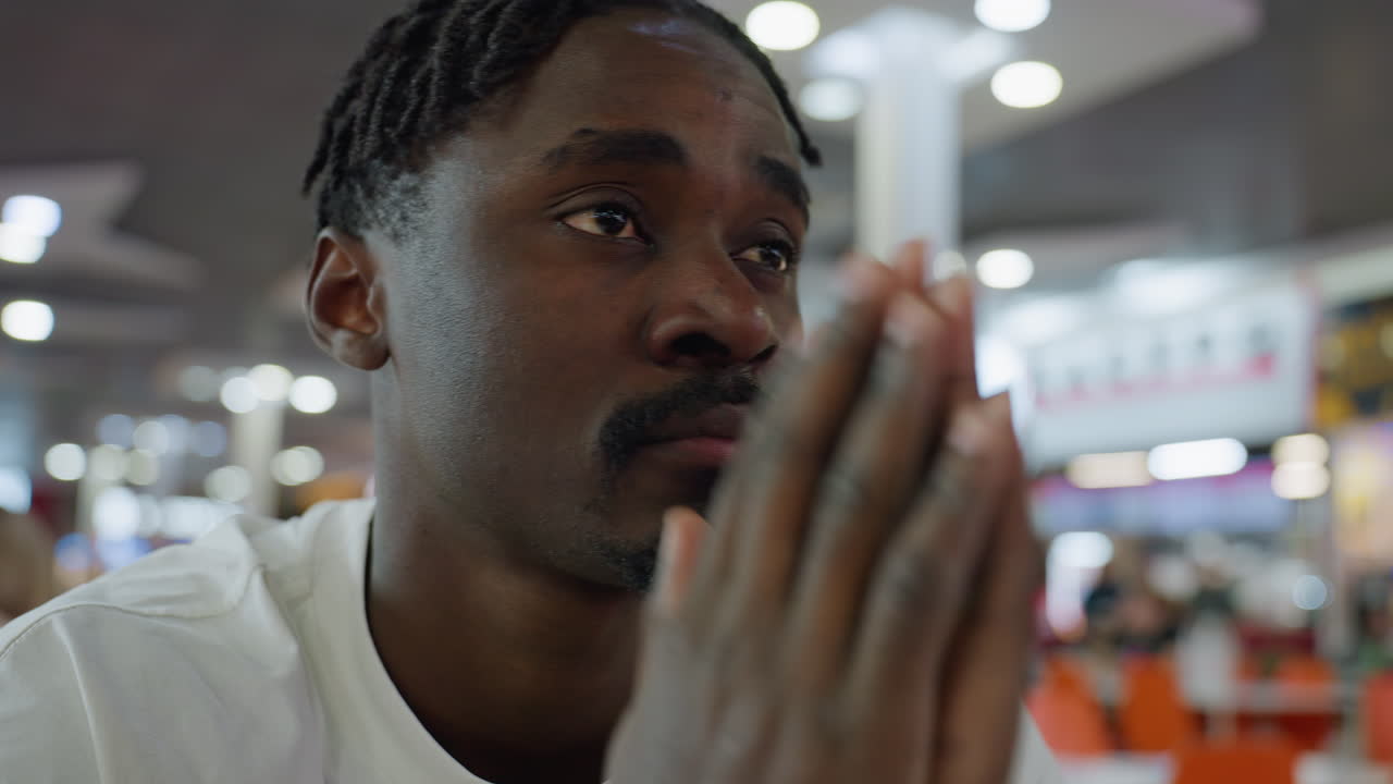 Estudiante sentada en un restaurante concurrido que muestra signos de agotamiento con los ojos en blanco y los labios apretados por la frustración mientras junta las manos, rodeada de gente en un fondo borroso