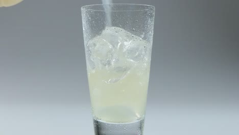 pouring lemonade into ice cube glass, fizzy citrus drink in slow motion