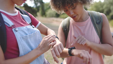 young caucasian woman and biracial woman check their fitness trackers outdoors