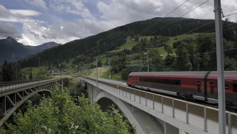 tren de pasajeros pasando por un puente en las montañas