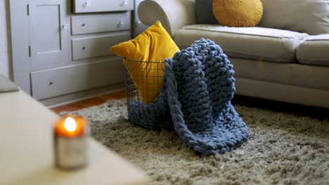 metal basket with pillow and warm hand knit blanket, cozy living room with lit candle on table - static shot