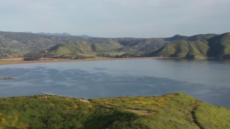 Drone-shot-orbiting-beautiful-yellow-wildflower-covered-mountain-top-and-large-lake-reservoir-during-the-California-super-bloom