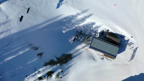 Aerial bird’s eye view of a ski chair lift ascending a snow-covered mountain, gliding above pine trees, ski runs, and fresh powder in a calm and breathtaking alpine setting