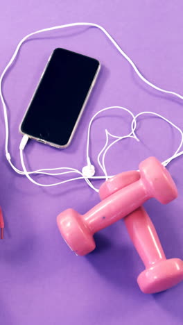 teléfono móvil con auriculares, zapatos y pesas en la mesa