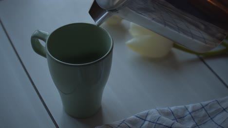 pouring fresh tea into mug on wooden table with white tulip flower, close up view