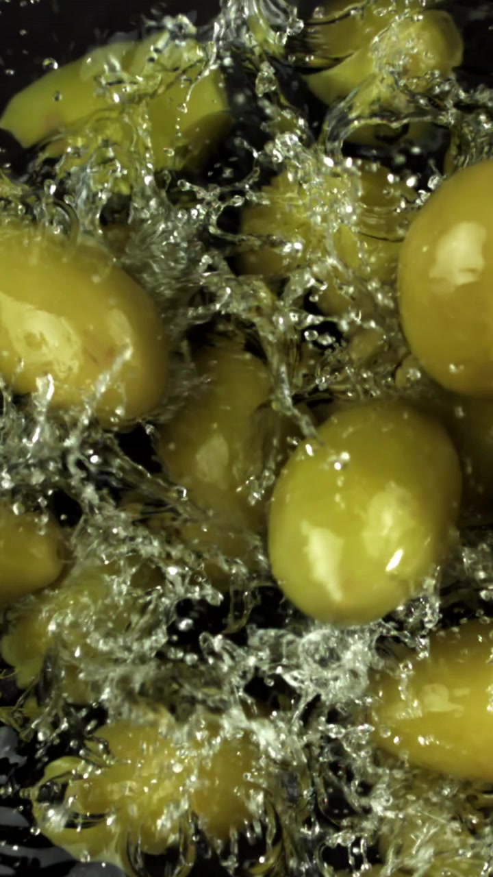 Olive verdi fresche che schizzano nell'acqua, al rallentatore