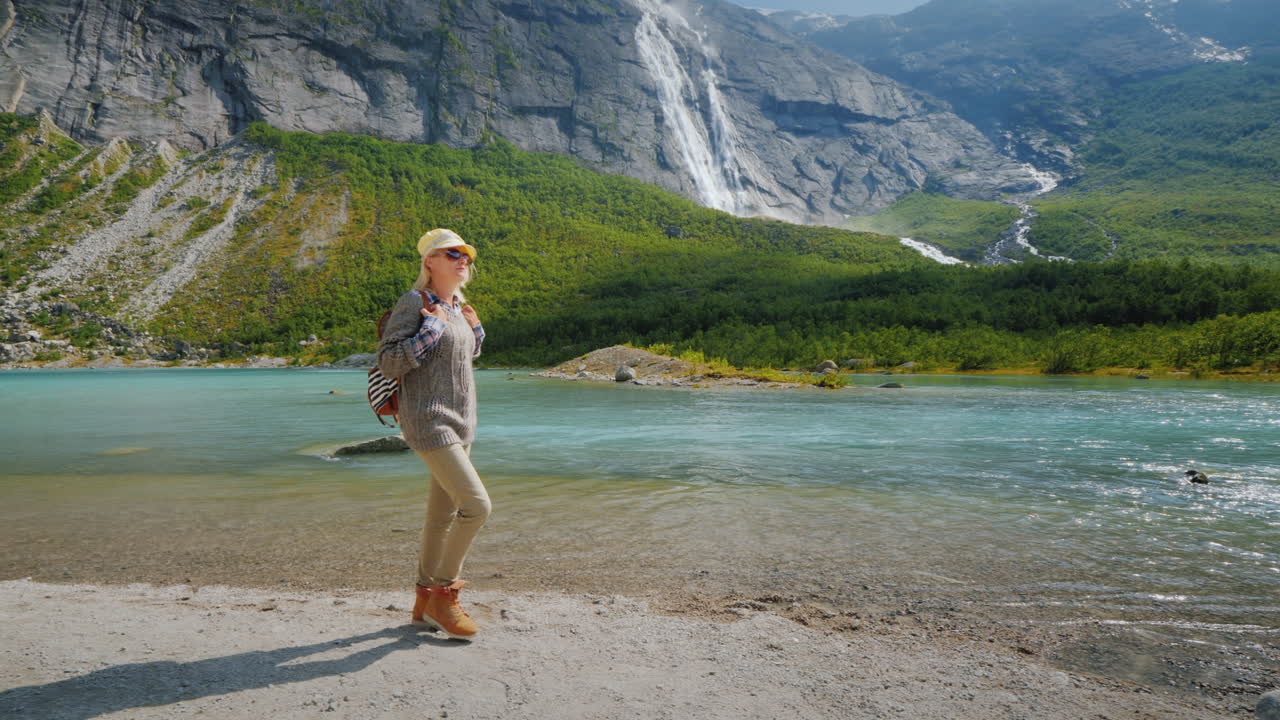 A Tourist Woman Walks Alone Surrounded By Majestic Nature - Mountains With Waterfalls On Top The Tra