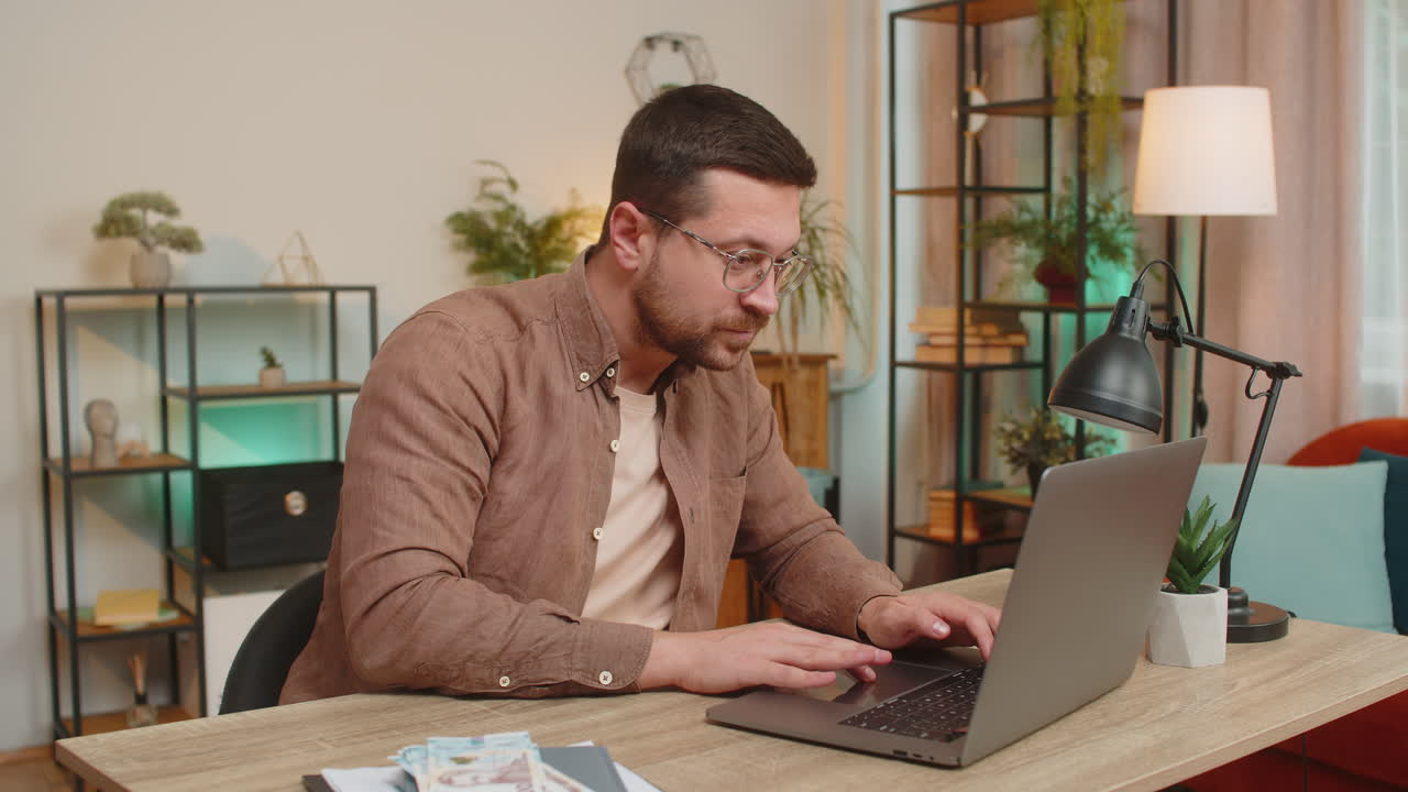 Rich happy caucasian man counting money hryvnias cash using laptop calculate domestic bills at home