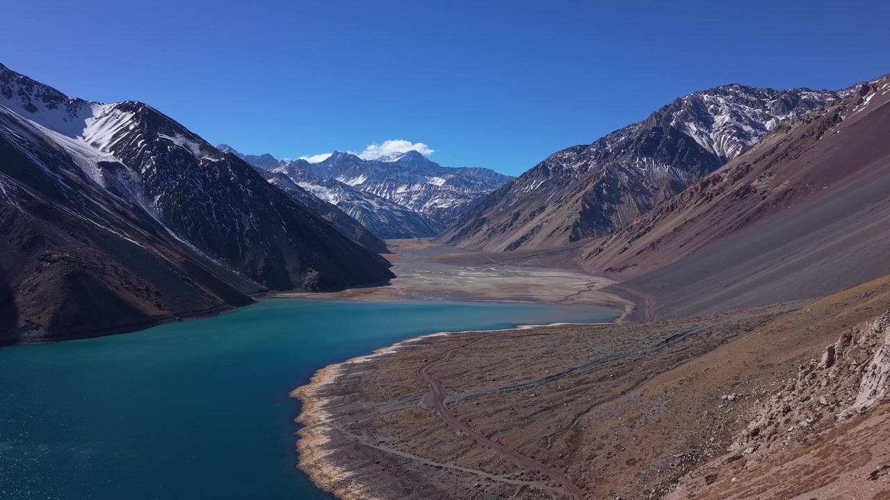 Volo in planata su acque glaciali turchesi che rivela un ampio delta di valle arida incorniciato da imponenti cime andine innevate. Embalse del Yeso, Cile.