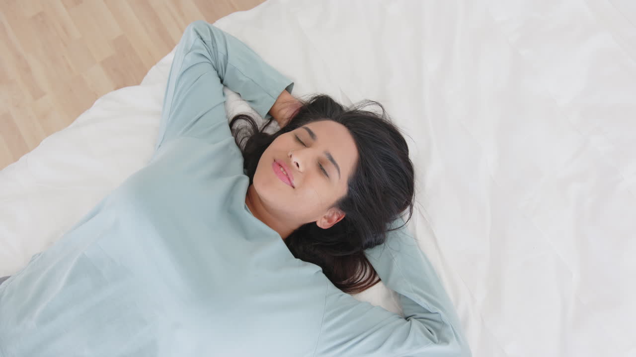 Relaxing on bed, mature asian woman smiling with eyes closed, enjoying spa day, at home