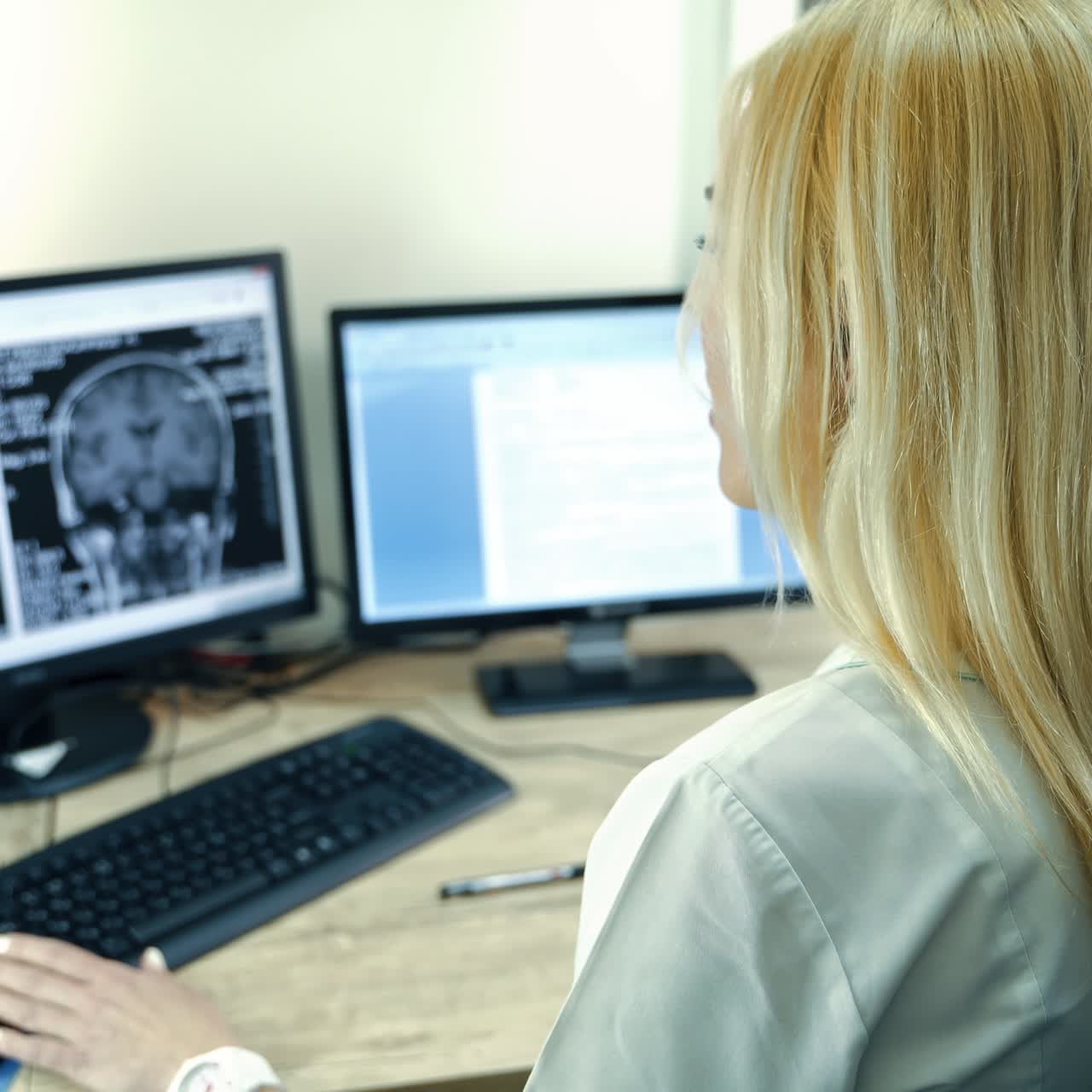 Rear view of a female lab technician sitting in front of computers. Medic looks at the MRI scan of head