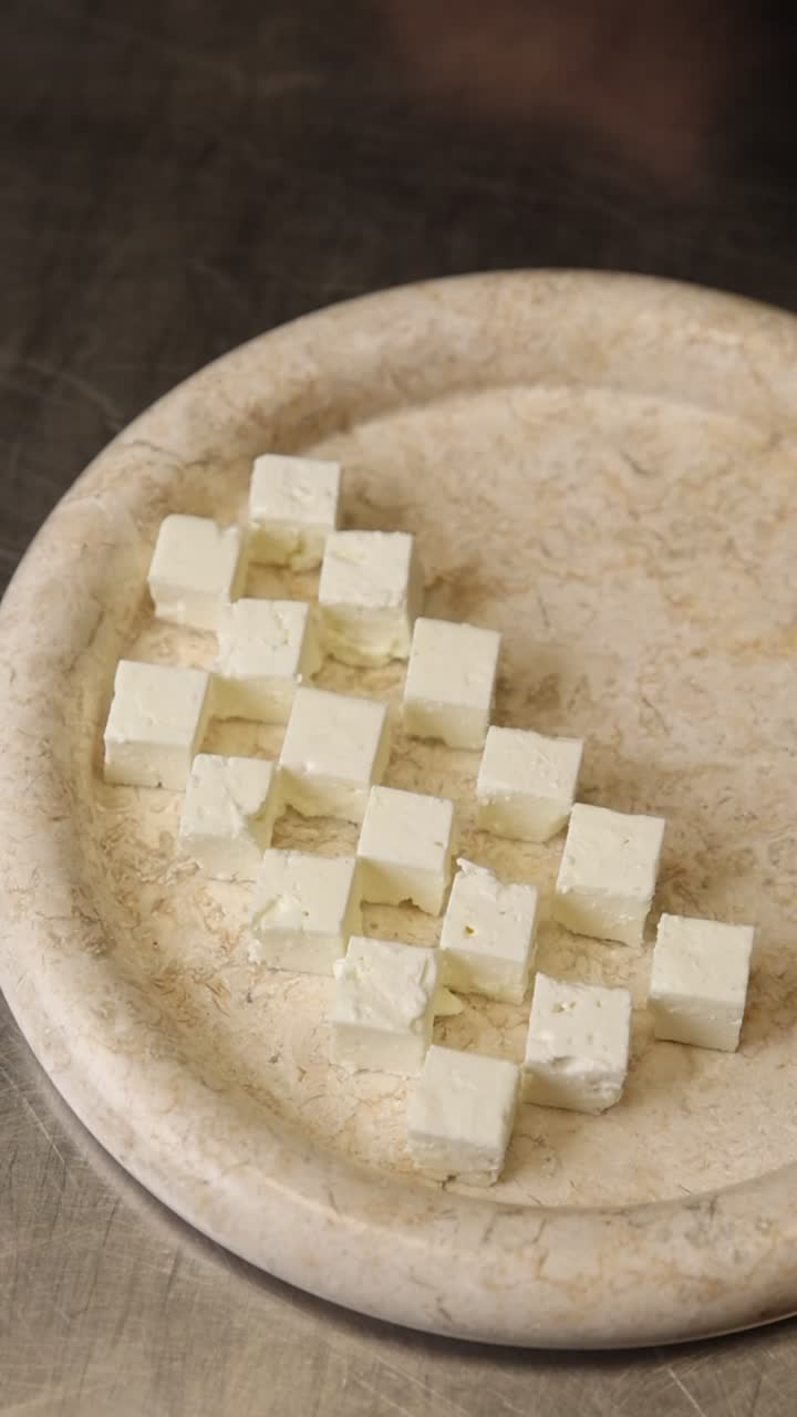 Main disposant des cubes de fromage blanc sur une assiette décorative