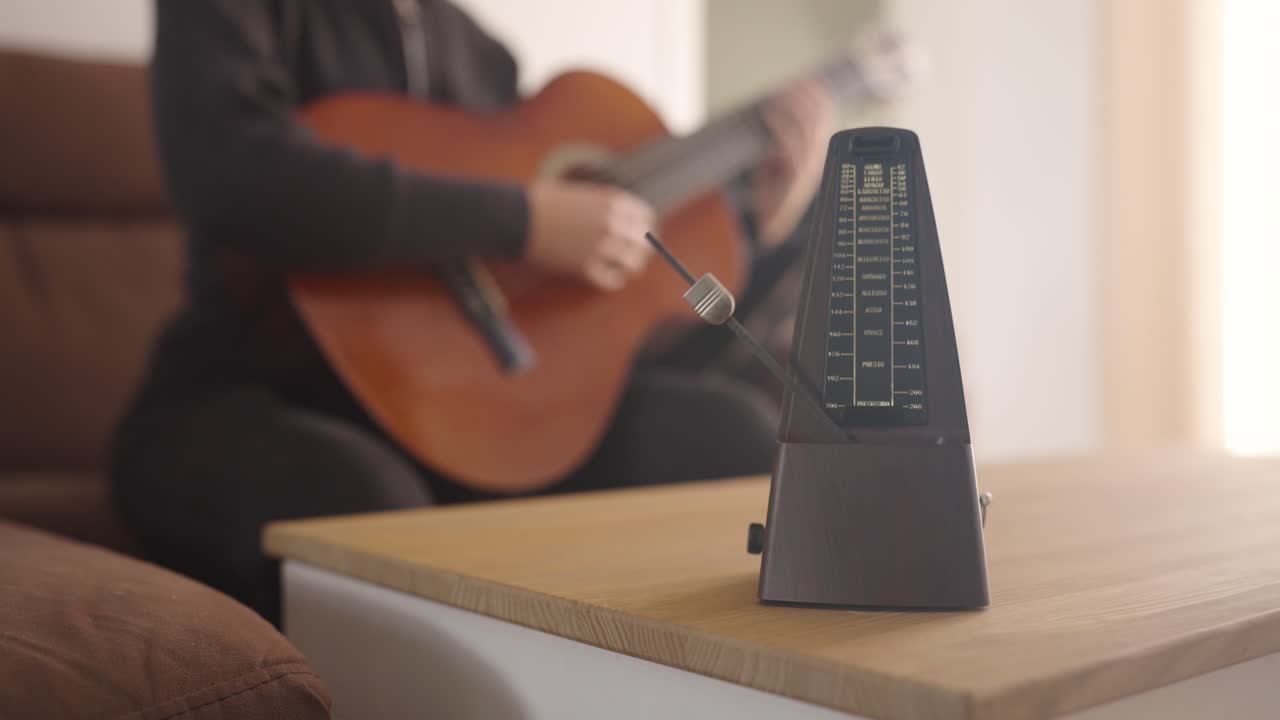 Musician playing acoustic guitar using a metronome for rhythm