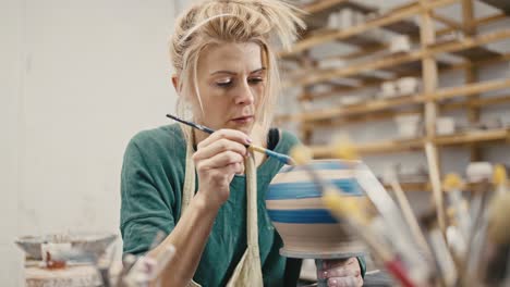 woman making ceramic item at workshop, painting handmade clay pot with brush and paint, slow motion