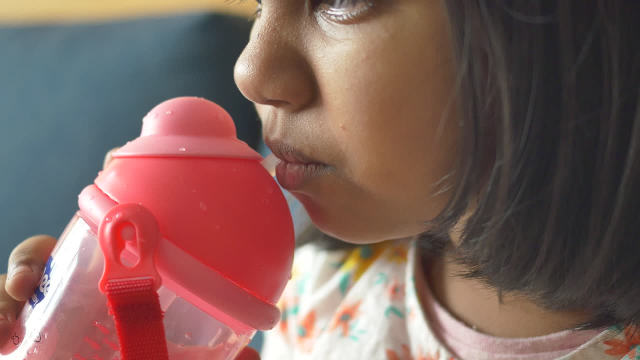 niña pequeña bebiendo de una botella de agua rosa