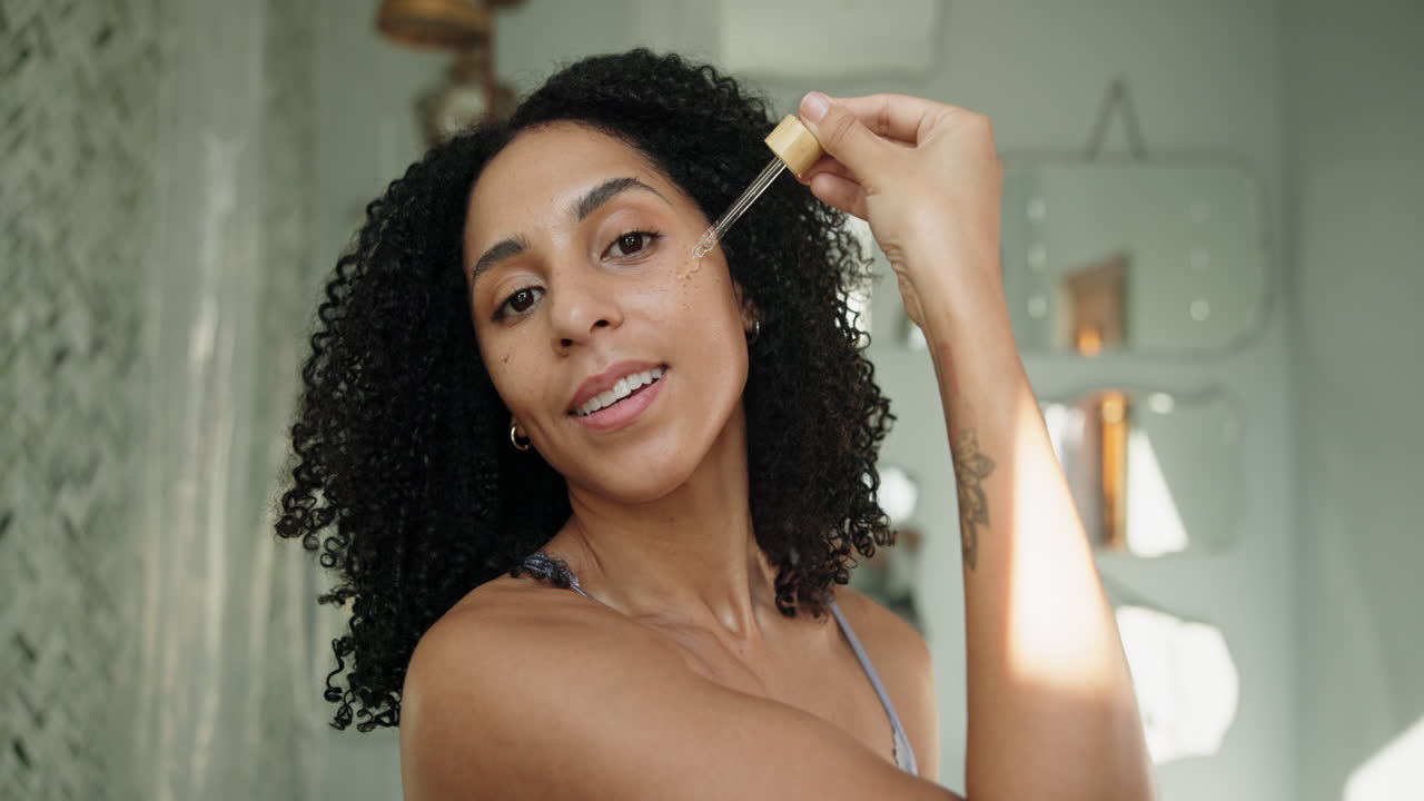 Mujer joven aplicando suero facial en la cara.