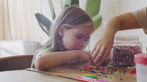 cerca de una linda niña rubia divirtiéndose jugando con cuentas de colores ayudada por su madre