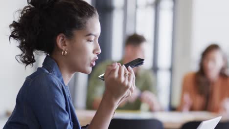 mujer de negocios casual biracial usando computadora portátil y hablando en teléfono inteligente en el escritorio, cámara lenta