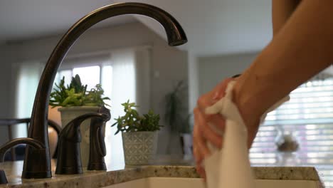 young man dries clean hands with paper towel at modern kitchen sink