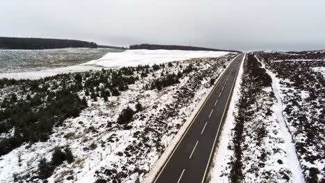 Antena-De-Largo-Camino-En-La-Distancia-A-Través-De-La-Campiña-Nevada-De-Las-Tierras-Altas-Tire-Hacia-Atrás-En-Aumento