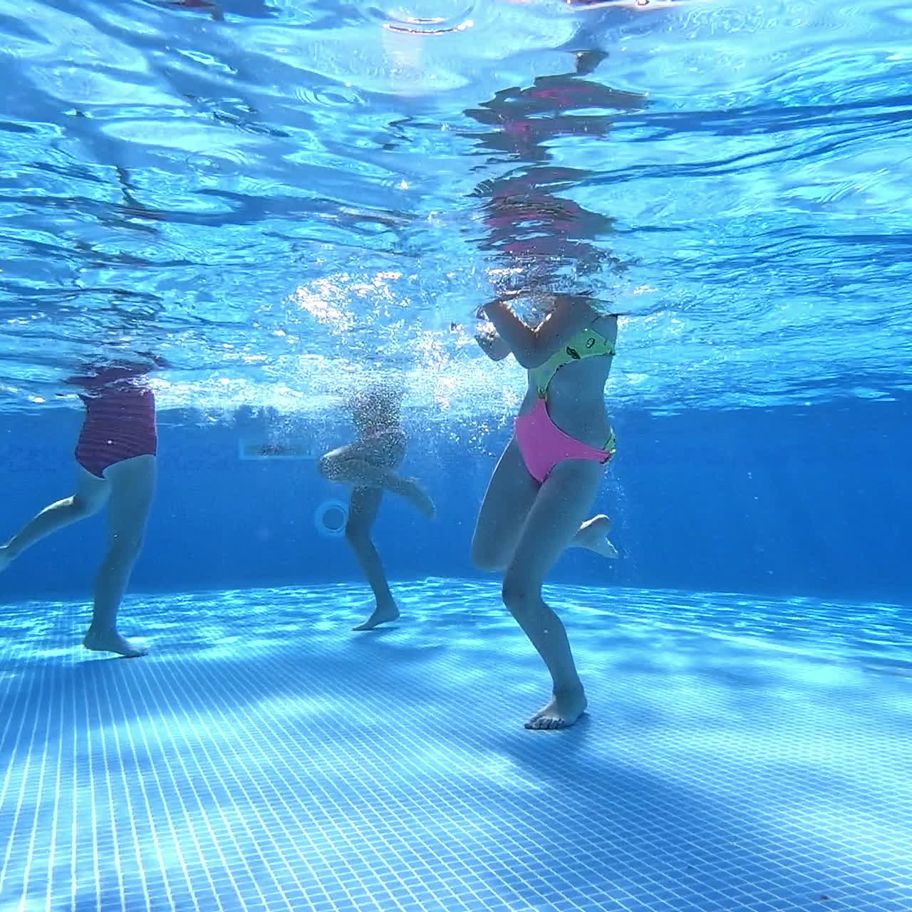 Underwater shot of girls legs playing in the pool. Children walking and waving their legs inside the swimming-pool. Clear view from underwater.