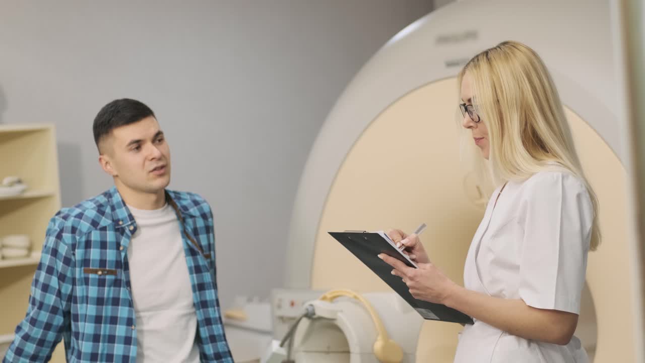 la radióloga tiene un diálogo con el paciente joven, pregunta y toma nota del historial médico del paciente, las quejas en la clínica moderna junto con la mri de tipo cerrado moderna