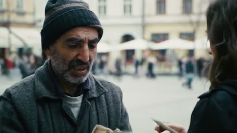 a man wearing a hat speaks with a woman in casual clothing at a lively city square filled with pedestrians. the sun begins to set in the background, creating a warm atmosphere.