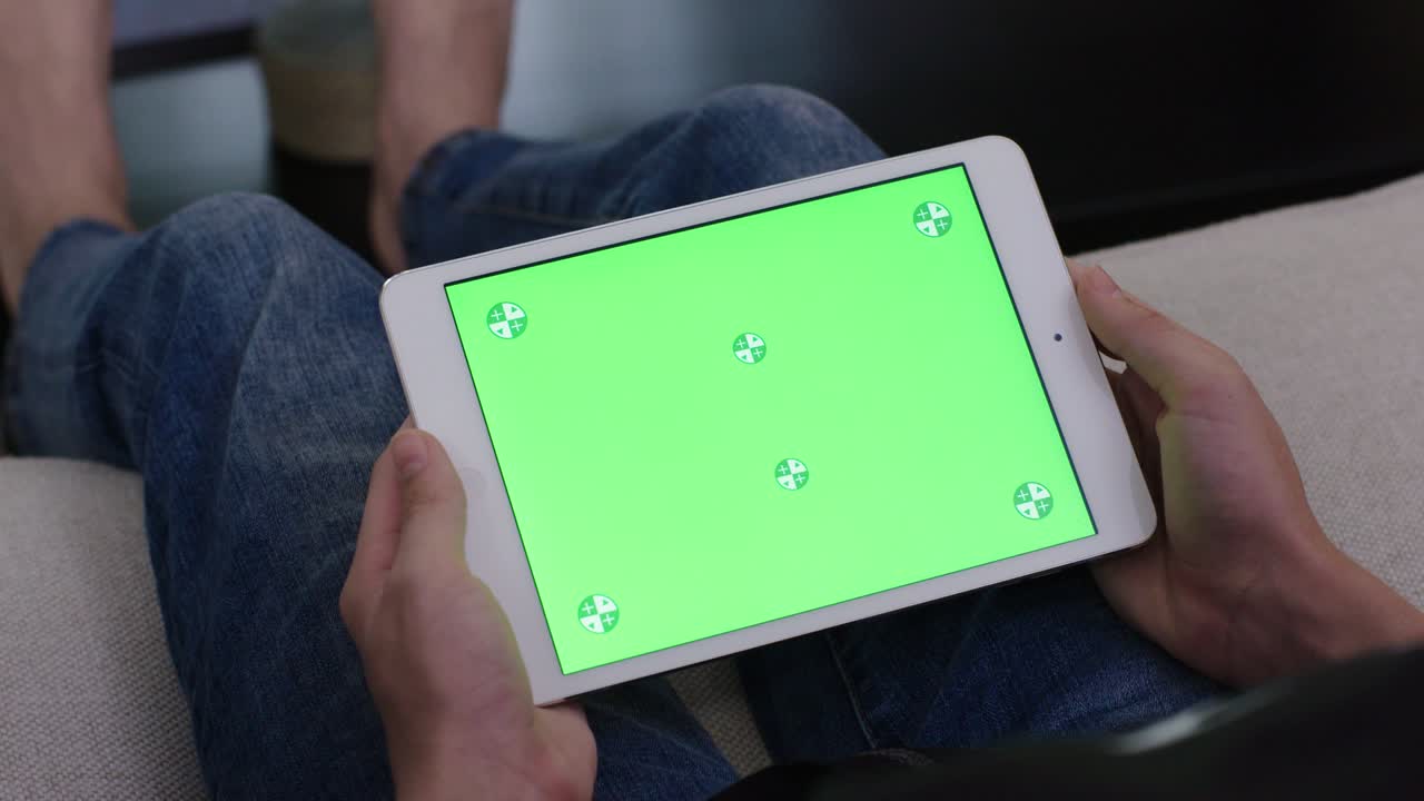 hombre joven sentado en el sofá, adolescente masculino en casa usando un dispositivo móvil para la tarea. tableta monitor de computadora pantalla verde para internet.