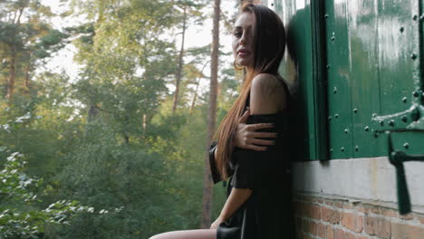 morena con un vestido negro, posando en un parque nacional, rodeada de árboles, una pared de ladrillos y una puerta verde