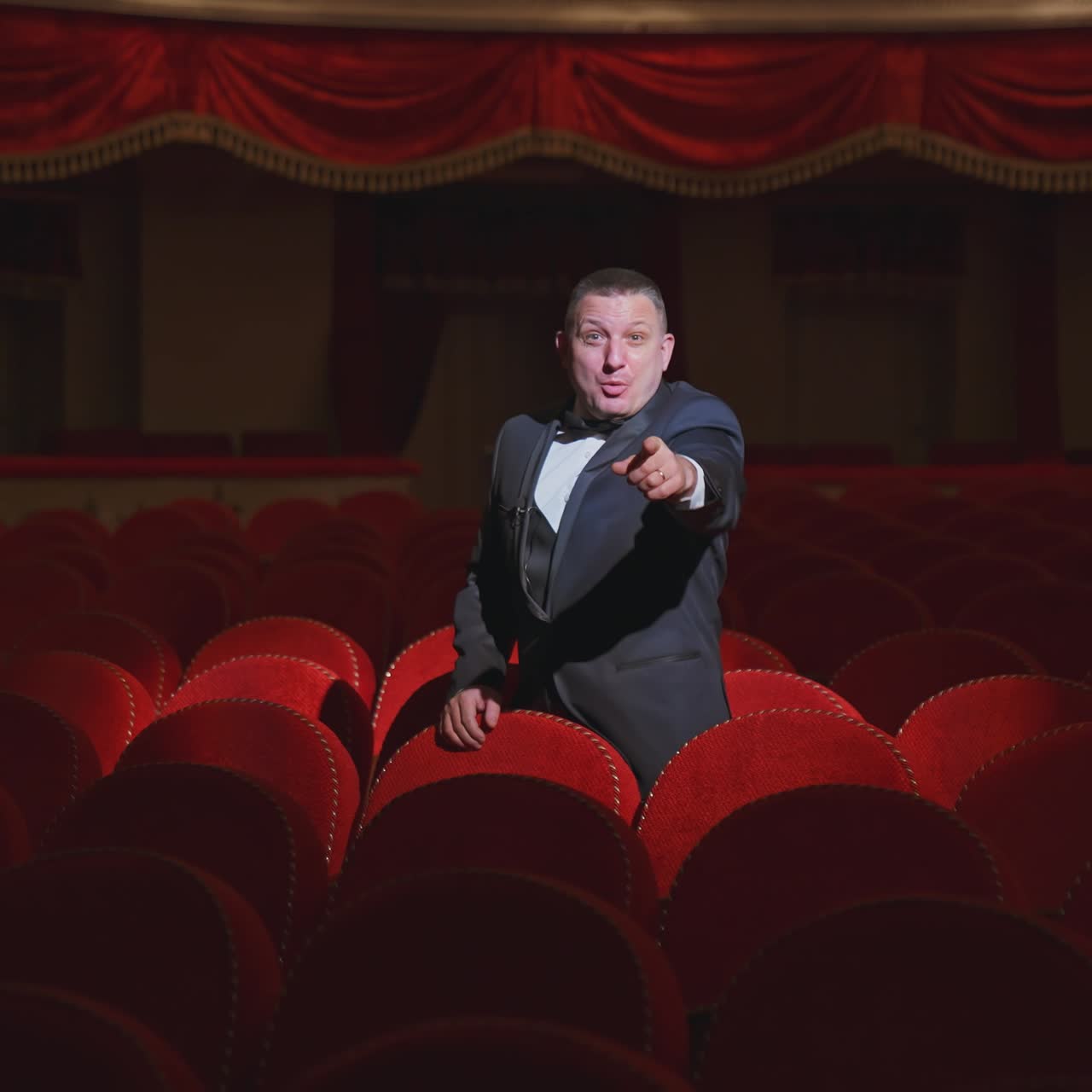 Man in empty theater. Rich man in suit taking off facial mask and says something among rows of red seats in the theater without audience. World crisis at pandemic.