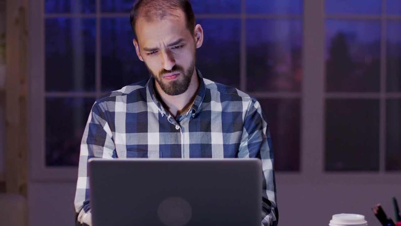 Uomo concentrato che lavora al laptop nel suo home office di notte
