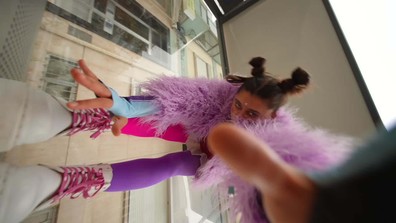 Ung kvinde i et farverigt lilla og lyserødt outfit poserer og danser
