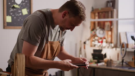 worker in apron takes photo of handmade wallet in studio