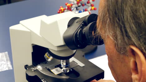 un profesor universitario de ciencias mirando a través de un microscopio células cancerosas humanas en un aula de laboratorio de biología