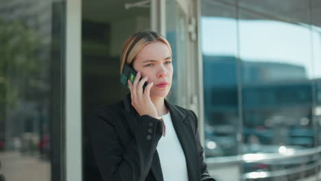 elegant woman with thoughtful expression conversing over phone with business associate while exiting conference meeting, holding door open, dressed in formal attire, with urban environment