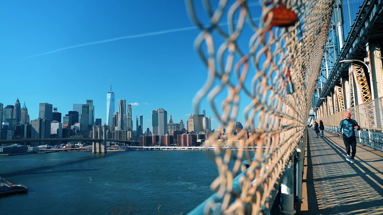 New York, USA, 1 aprile 2026: Jogger che corre lungo il percorso pedonale del Ponte di Manhattan. Un corridore passa sotto le travi d'acciaio mentre lo skyline di Manhattan si estende sul porto