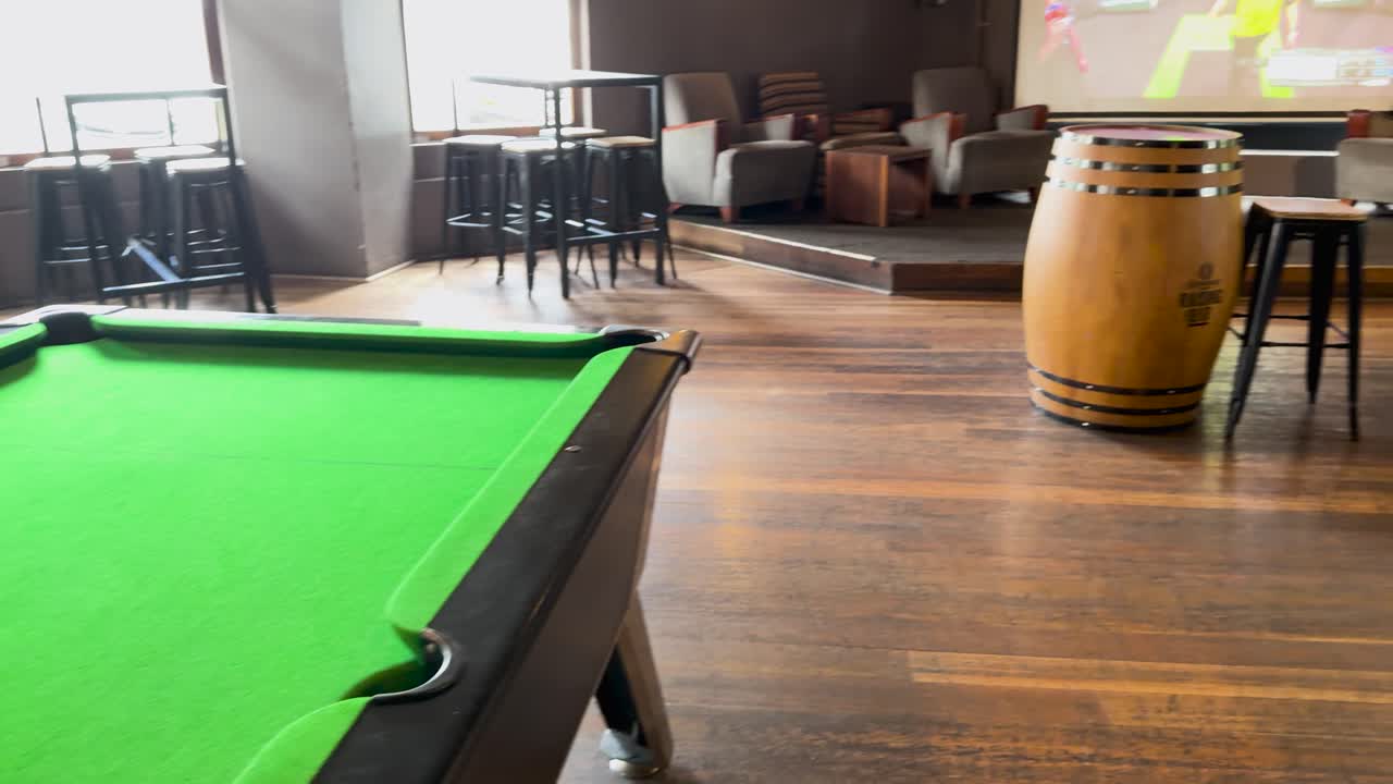 A snooker table in a sports bar with wooden floors and ambient lighting. The room is empty, creating a calm atmosphere