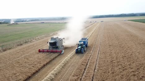 Eine-Filmische-4K-Drohnenaufnahme-Eines-Mähdreschers-Und-Eines-Traktors-Bei-Der-Ernte-Eines-Feldes-In-Frankreich,-Die-Die-Landwirtschaft-Mit-Einer-Epischen-Aussicht-Und-Dramatischem-Staub-Zeigt