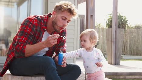 young white dad and toddler daughter blow bubbles outdoors