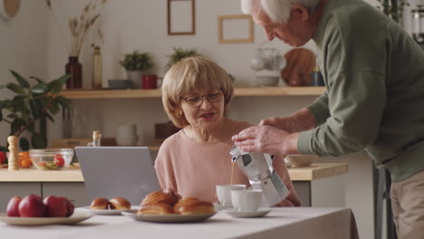 senior couple drinking coffee and speaking in kitchen