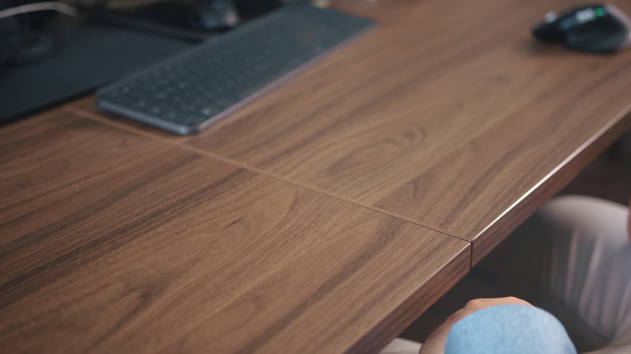 hombre con camisa azul empuja el teclado gris en un escritorio de madera