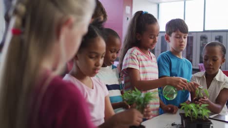 Diverse-group-of-happy-schoolchildren-looking-after-plants-in-classroom-during-nature-studies-lesson